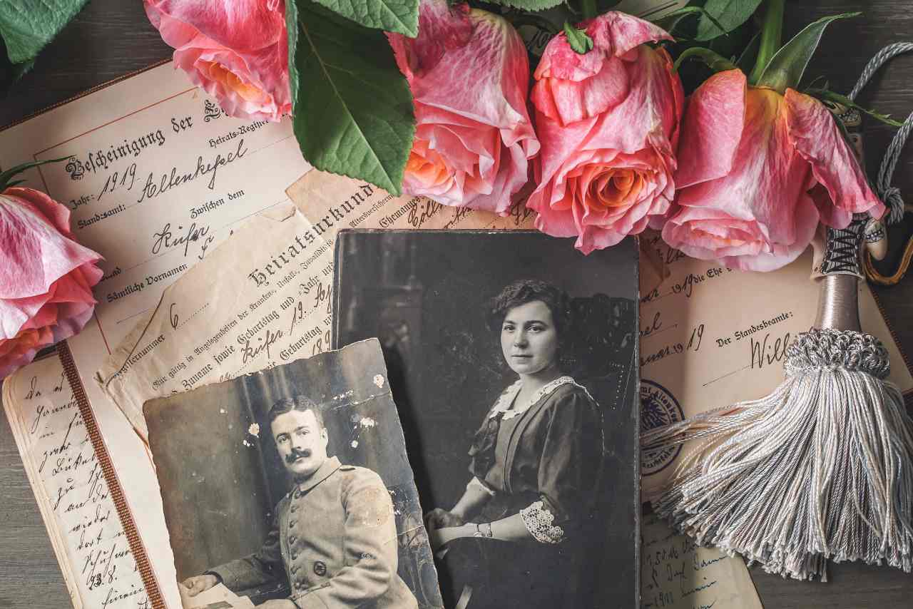 Vintage photos of people with old documents laid behind the photos. Pink flowes and a tassel surround the photos and documents.