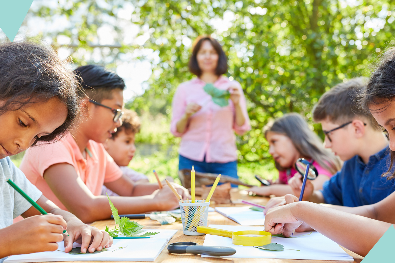Kids working on a project outside while a teacher helps.
