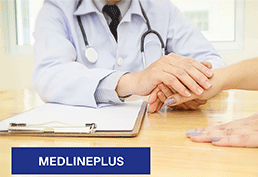 doctor comforting a patient by holding their hand at a desk. The desk has a clipboard on it. 