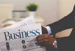 arms of man in a suit with an expensive watch holding a newspaper with the headline reading Business