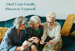 three older women with grey and white hair sit on a turquoise velvet couch in elegant outfits looking at old photos. 