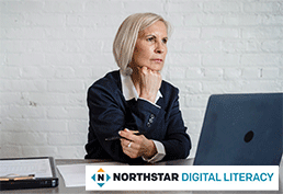 Older woman with grey hair resting her head on her fist looking over a laptop screen. 