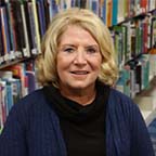 Board Member Elizabeth Miller sitting in front of a bookshelf of books