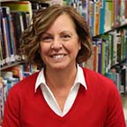 Board President Mary Burns sitting in front of a bookshelf of books