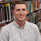 Board Member Tony Yoder sitting in front of a bookshelf of a book