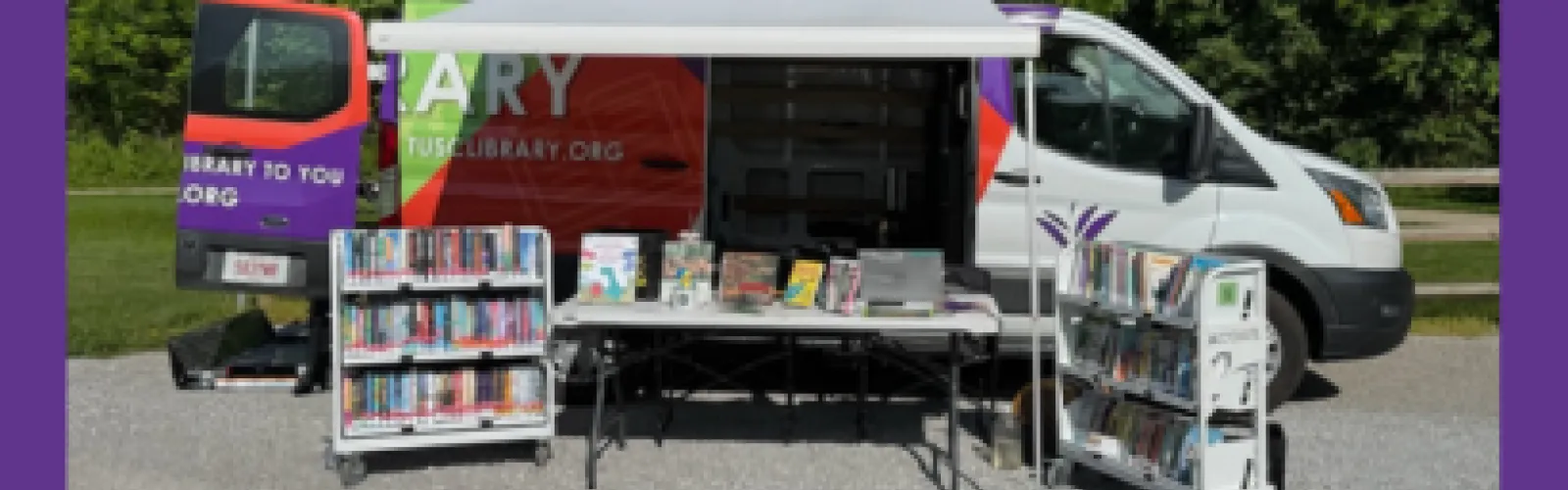 A Mobile Services vehicle with open sides and rolling carts out front and a table with a laptop on it.
