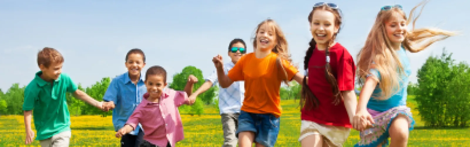 Three girls and four boys dressed in bright summer clothes running through a field of dandelions. 