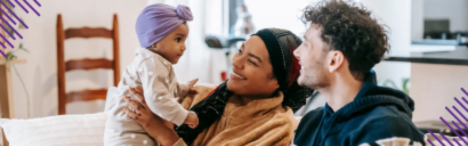 Photo of a mom holding her baby while sitting on a couch next to the baby's dad. 