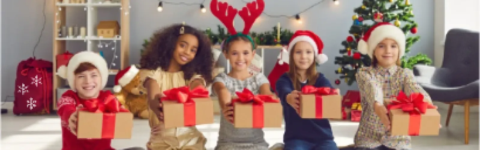 Five diverse children holding out Christmas presents in front of a Christmas backdrop. 