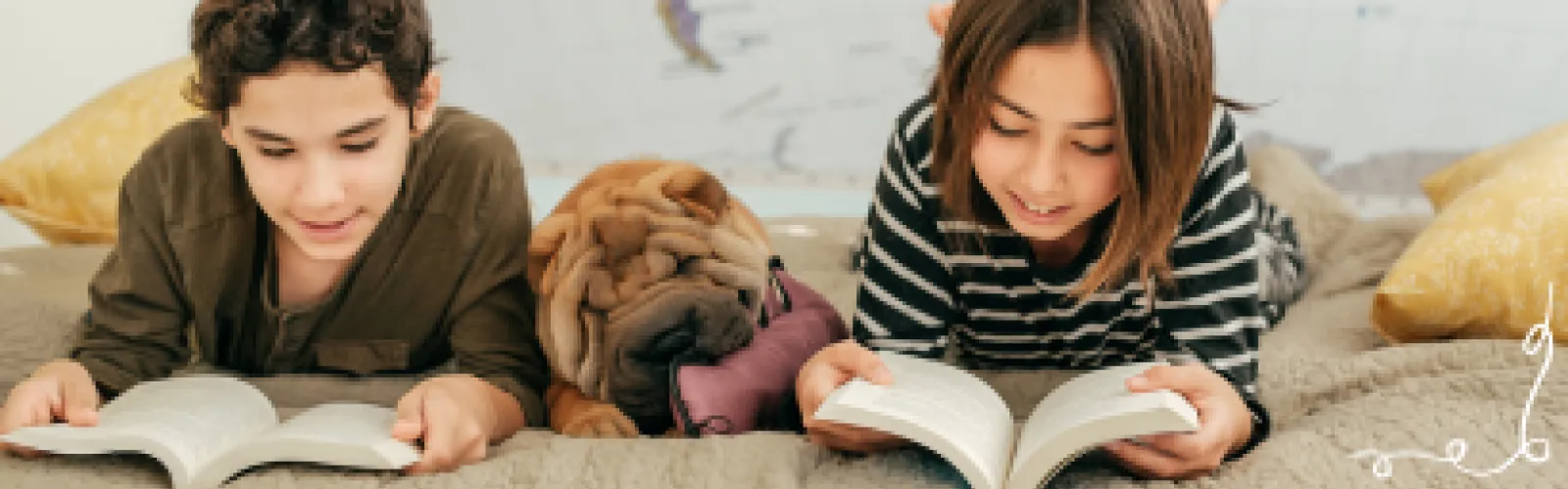 A boy and girl laying on their stomachs reading books with a sharpee dog laying between them. 
