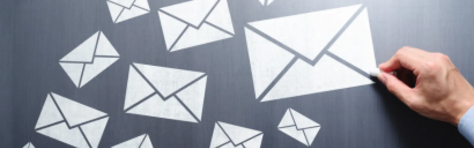 Hand drawing envelopes on a chalkboard with white chalk.