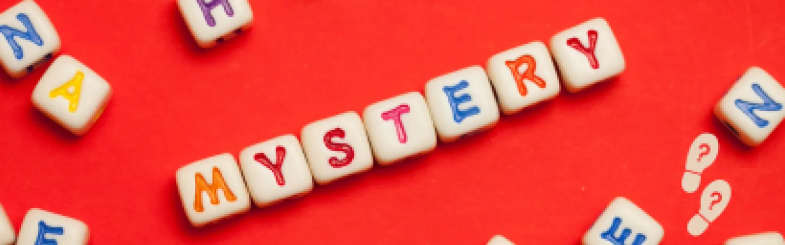 Lettered dice rolled on a red table to spell the word mystery. 
