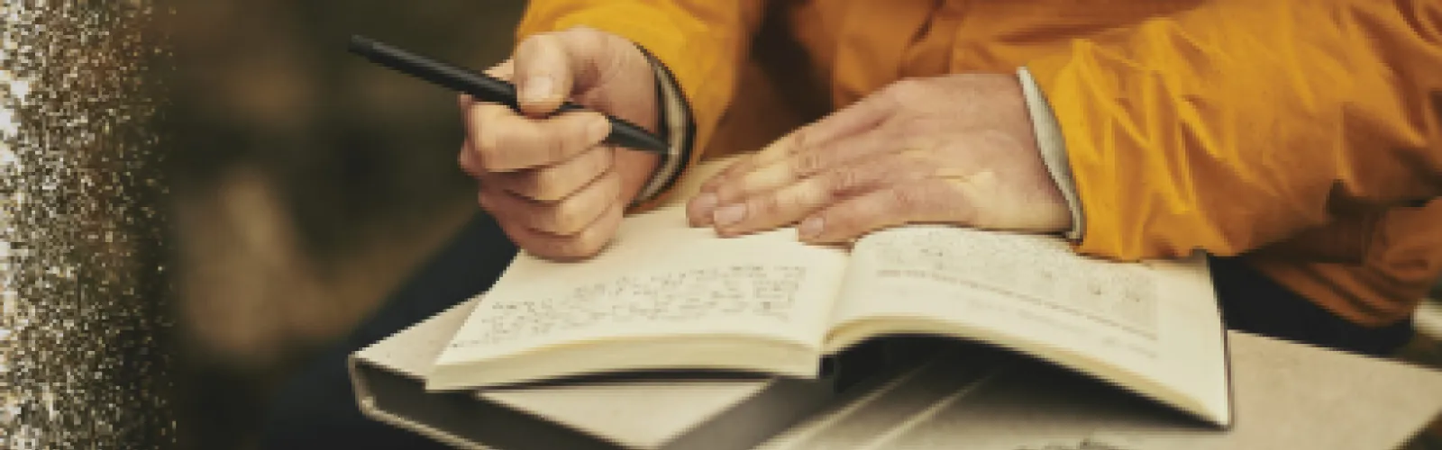 Person wearing a yellow sweater writing in a journal on their lap. 